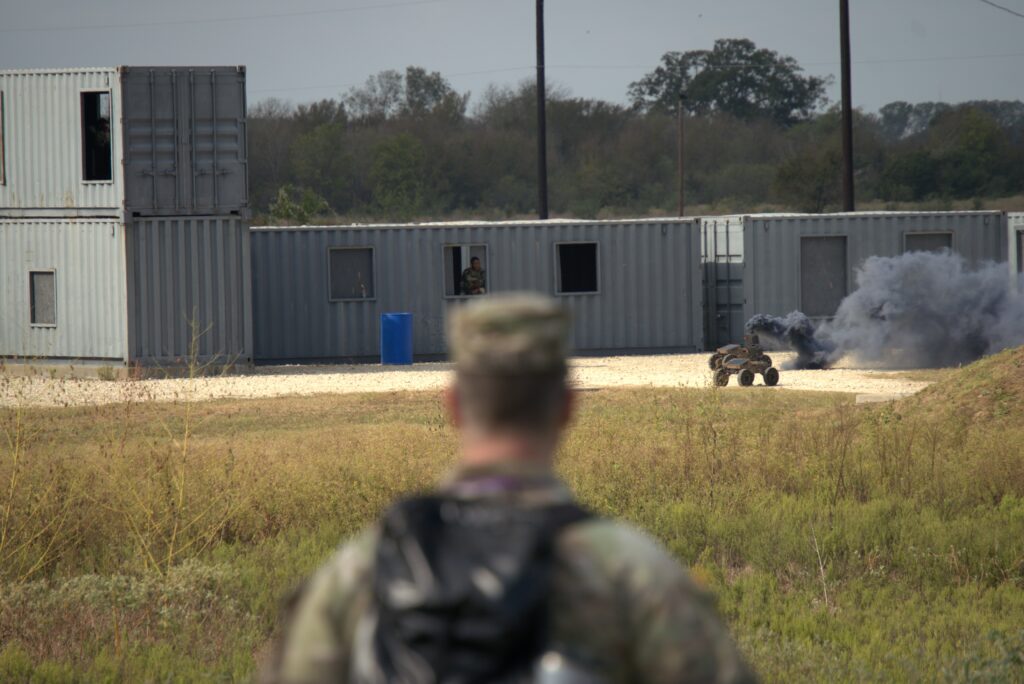 Soldier observing a wheeled unmanned vehicle deploy smoke.