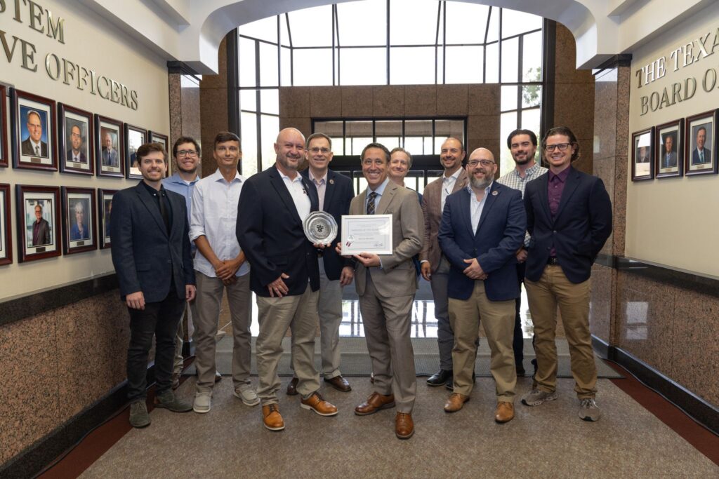 11 Men Standing in a hallway, Chancellor Glenn Hegar presenting the Employee of the Quarter award to Kevin Brown.